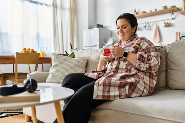 A beautiful young plus sized woman relaxes on a soft couch while savoring a warm beverage.