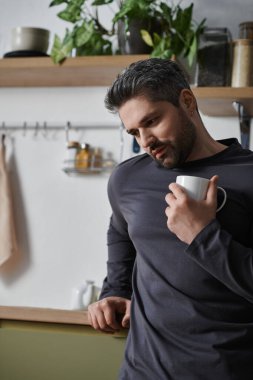 Sıcak bir mutfakta yakışıklı bir adam yeşilliklerle çevrili hayatı düşünürken kahvesini yudumluyor..
