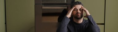 Yakışıklı bir adam, parlak bir mutfak zemininde oturur, derin düşüncelere dalmış, odaklanmış bir ifadeyle..