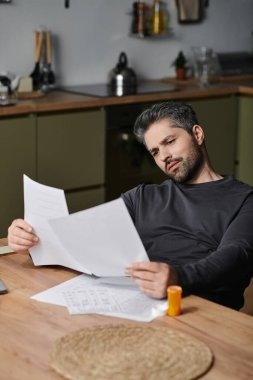 Yakışıklı bir adam, iyi düzenlenmiş bir mutfak masasında basılı kağıtları okuyor..