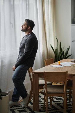 Güneş ışığı sıcacık boşluğu doldururken, düşüncelere dalmış yakışıklı bir adam pencerenin kenarında duruyor..