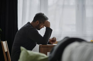 Yakışıklı bir adam derin düşüncelere dalmış, elinde bir bardak, dalgın dalgın dalgın dalgın oturuyor..