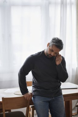 Şık bir adam, düşüncelere dalmışken bir telefon görüşmesine dalmış bir şekilde masanın başında duruyor..