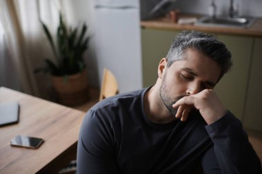 A thoughtful man rests his chin on his hand, surrounded by a tranquil kitchen setting. clipart