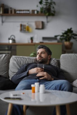 Yakışıklı bir adam rahat bir şekilde kanepede uzanıyor, şık bir oturma odasında içkisinin tadını çıkarıyor..