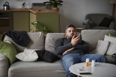 Yakışıklı adam rahat bir şekilde rahat bir koltukta uzanır, sakin bir yerde akıllı telefonuna odaklanır..