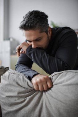 Düşünceli bir adam, sakin ve rahat bir çevreyle çevrili, derin bir tefekkür içinde bir kanepeye yaslanır..