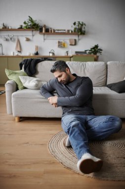 Yakışıklı bir adam modern, rahat bir salonun zemininde düşünceli bir şekilde oturur..