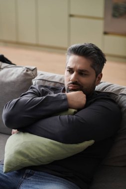 Yakışıklı bir adam düşünceli bir şekilde kanepede oturur, sakin bir öğleden sonra yastığı yakın tutar..