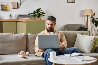 Odaklanmış bir adam kahvesini yudumlarken şık bir yaşam alanında dizüstü bilgisayarıyla meşgul olur..