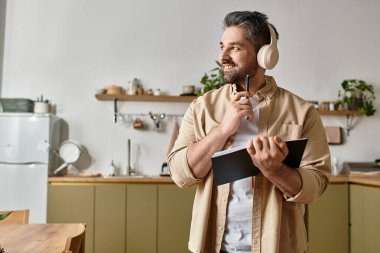 Kulaklıklı gülümseyen bir adam, sıcaklıkla çevrili defterine düşünceli bir şekilde yazar..