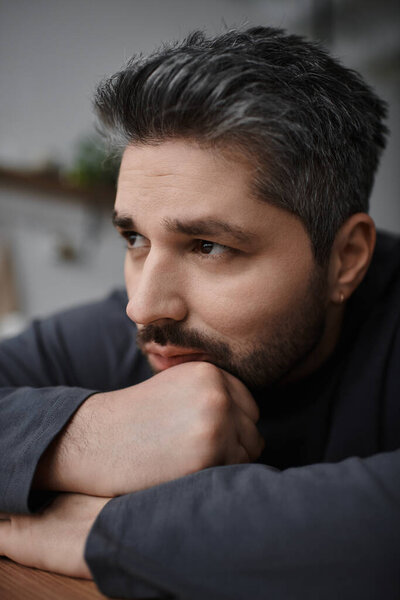 Красивый мужчина выглядит заботливым, положив подбородок на руку в теплой обстановке.