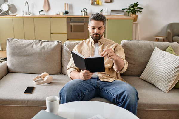 A handsome man enjoys a quiet moment reading a book on a comfortable sofa in his home.