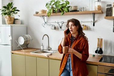 Bir kadın sıcak bir mutfakta elinde bardak tutarken duygularını telefonda paylaşıyor..