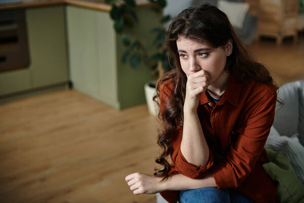 Женщина сидит в уютной комнате, размышляя о своей печали и изоляции..