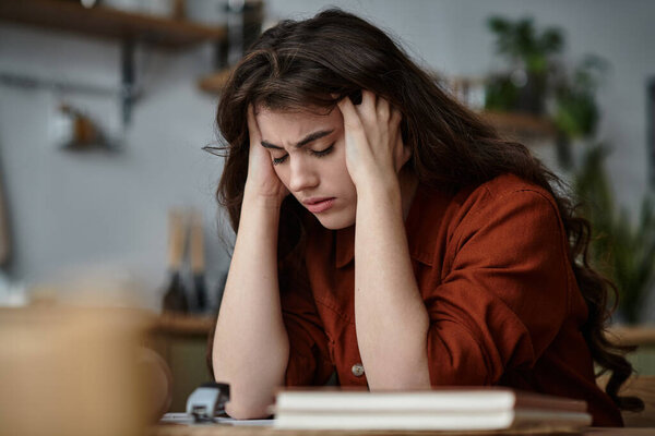 Женщина сидит за деревянным столом, переполненная чувствами депрессии, глубоко погружённая в мысли.