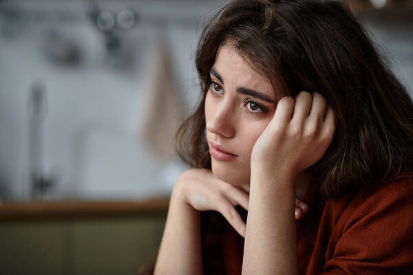 Женщина кажется потерянной в мыслях, выражая глубокие эмоции в теплой, уютной атмосфере.