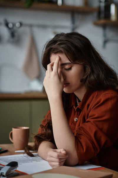 A woman displays her feelings of sadness and overwhelm while sitting at a wooden table.