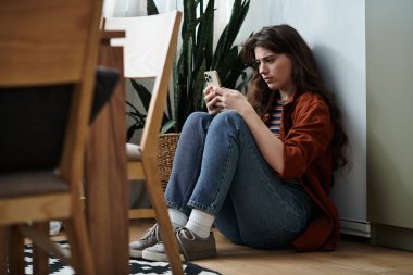 Yerde oturan bir kadın telefonuna bakarken duygularını derin derin düşünür..