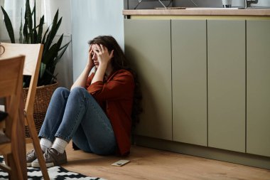 Overwhelmed by emotions, a woman sits on the floor, seeking comfort within her quiet space. clipart