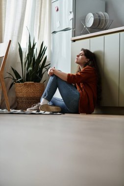 Mutfak zemininde bir kadın oturuyor, derin bir düşünce ve yalnızlık içinde..