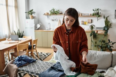 A woman battles her feelings as she sorts clothes in a bright, serene room filled with plants. clipart