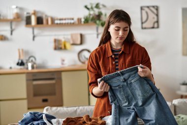 Genç bir kadın, rahat bir mutfak alanında giysilerini düzenlerken duygularını yansıtır..