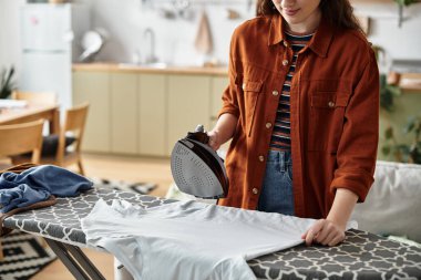 A woman presses clothes in her cozy kitchen, displaying her struggle with inner feelings. clipart