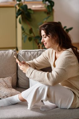 A woman sits peacefully on a couch, deep in thought while using her phone. clipart