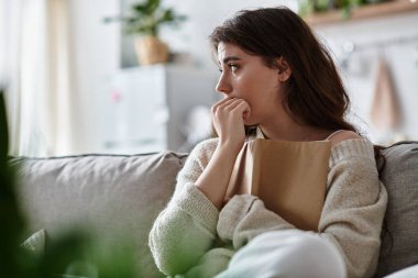 Kanepede oturan bir kadın, düşüncelere dalmış, duygularını yansıtıyor ve depresyonla mücadele ediyor..