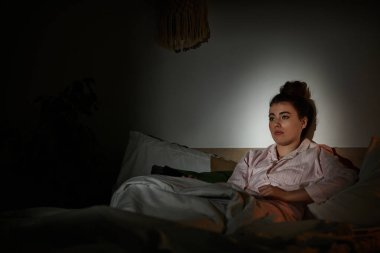 Bir kadın gece yatağında oturur, yalnızlık ve içgözlem hisleriyle boğulmuş..