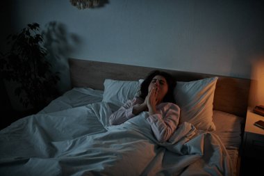 Bir kadın gece yatağında oturur, derin üzüntü ve iç gözlem duygularını ifade eder..