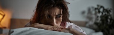 Gölgeler alacakaranlıkta etrafında dans ederken bir kadın, düşünceler içinde kaybolmuş yatağında oturuyor..