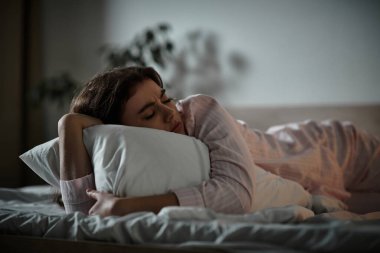 Bir kadın, kederli duygular hissederken yastığını tutarak yatağında yatar..