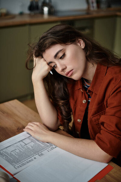 Молодая женщина сидит одна за кухонным столом, переполненная своими мыслями и эмоциями.