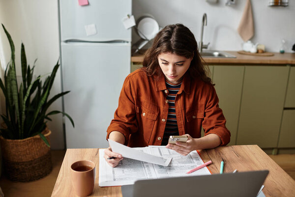 Женщина сидит за кухонным столом, погруженная в размышления, рассматривая документы..