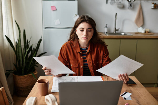 A young woman appears deep in thought, grappling with paperwork at her cozy kitchen table.