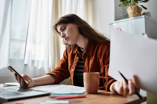 A young woman at a wooden table is distracted by her phone and papers, showing her turmoil.