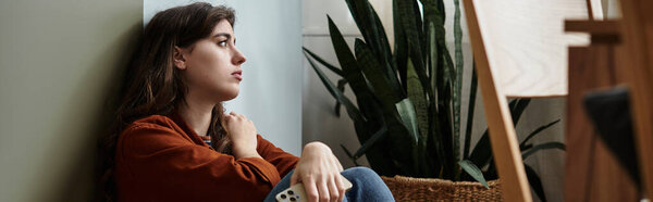 Женщина сидит у стены, задумчивая, окруженная комнатными растениями дождливым днем.