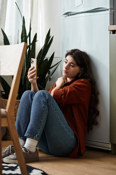 Женщина задумчиво сидит на холодильнике, ее эмоции видны, когда она смотрит на свой телефон.