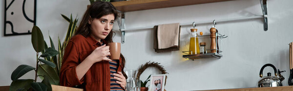 На теплой кухне женщина держит кружку, затерявшись в мыслях, размышляя о своем эмоциональном состоянии.