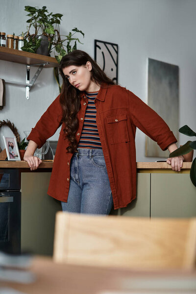 Женщина задумчиво стоит на теплой кухне, передавая глубокие эмоции и одиночество..