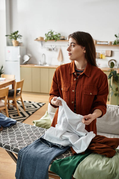 Женщина задумчиво стоит, складывая белье на своей уютной кухне, выражая свою внутреннюю борьбу.