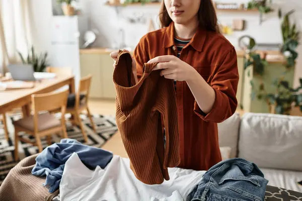 Düşünceli bir kadın, günlük zorlukları yansıtan rahat bir evde giysilerini katlar..