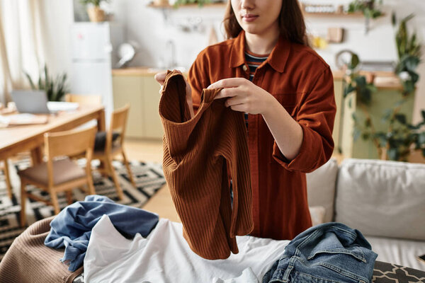 Задумчивая женщина складывает одежду в уютном доме, размышляя о повседневных проблемах.