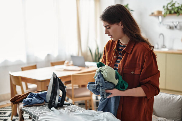 Женщина стоит в светлой комнате, обремененная прачечной, отражая свои эмоции.