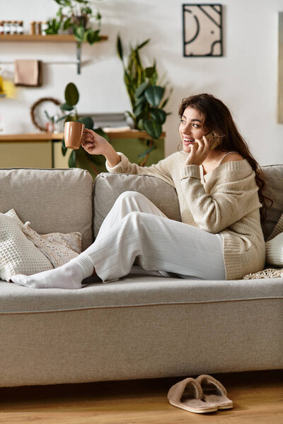 Женщина наслаждается радостным телефонным звонком, потягивая из кружки в уютной обстановке.