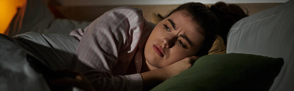 Женщина лежит в постели, переполненная чувством грусти и самоанализа в тускло освещенной комнате..