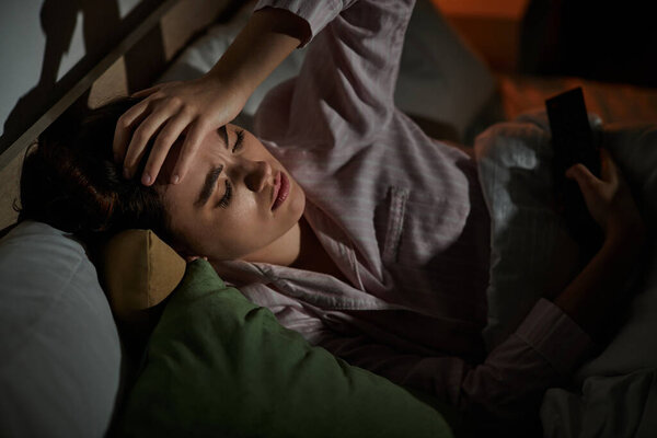 Женщина лежит без сна в постели, обремененная тяжелыми мыслями и эмоциями в тишине.