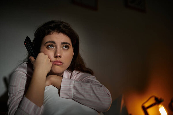 A woman sits alone in a dim room, lost in thought and grappling with her feelings.